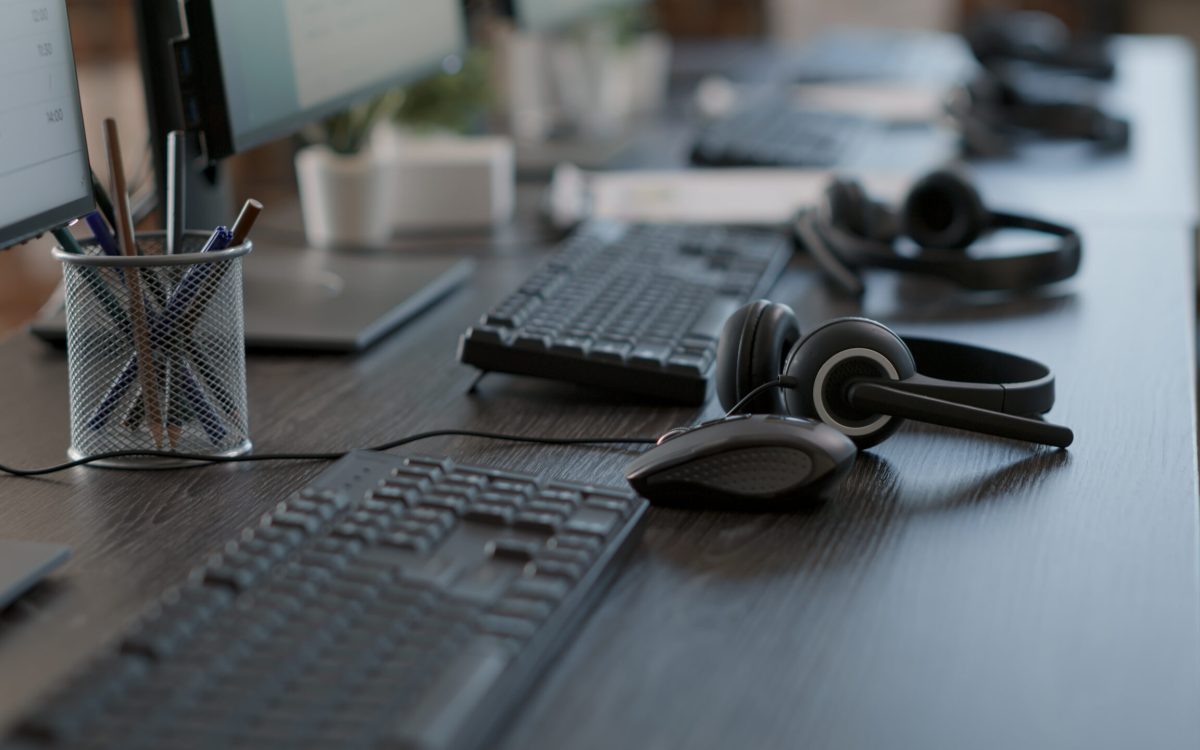 Audio headset used by call center agents to help clients and do telecommunication with technology. Empty customer service workstation with headphones, computers and modern gadgets.